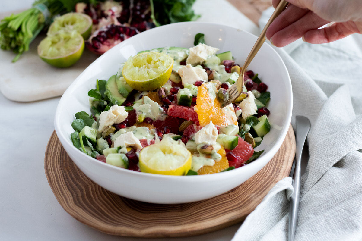 Un bol de salade d'agrumes colorée composée d'oranges, de pamplemousse, de citron, de citron vert et de grenade, arrosée d'une vinaigrette sans produits laitiers à base de coriandre...