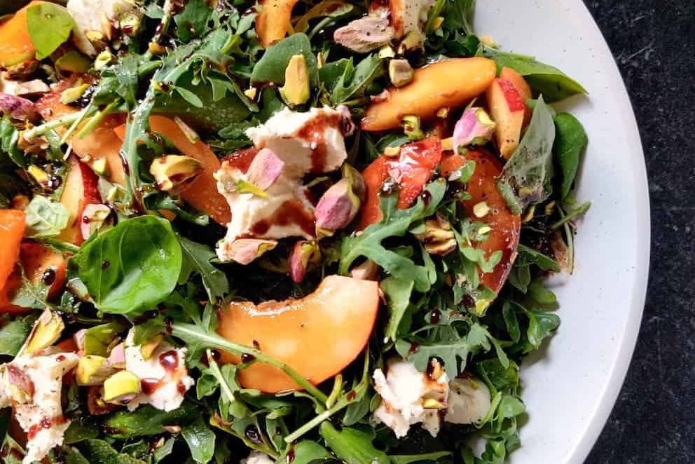 Une salade de légumes verts mélangés, de nectarines, de noix hachées et de fromage brie sans produits laitiers, arrosée d'une vinaigrette balsamique.