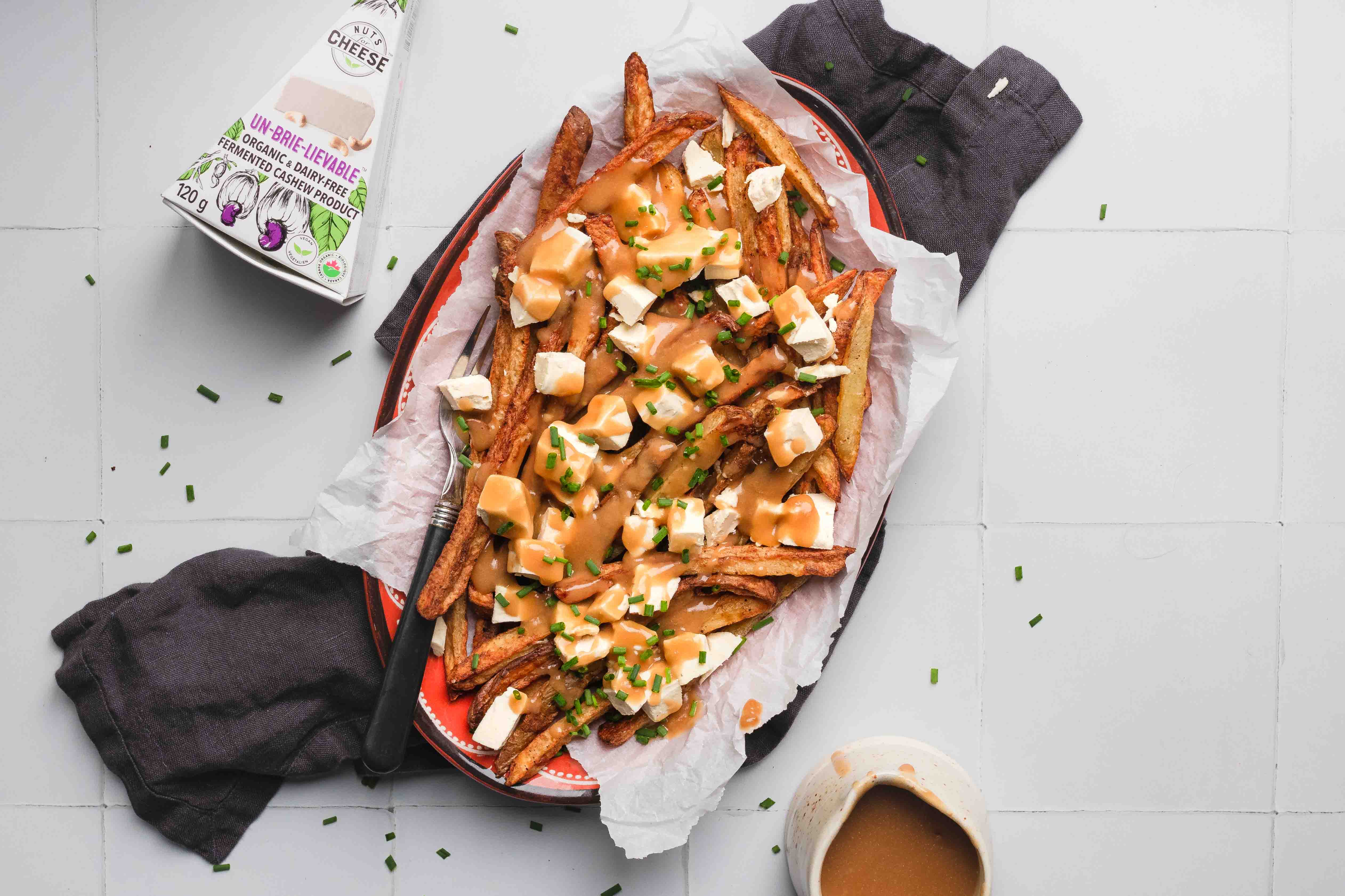 Plat préparé de poutine classique végétalienne à base de brie sans produits laitiers, présenté sur une serviette avec un accompagnement de sauce végétale.