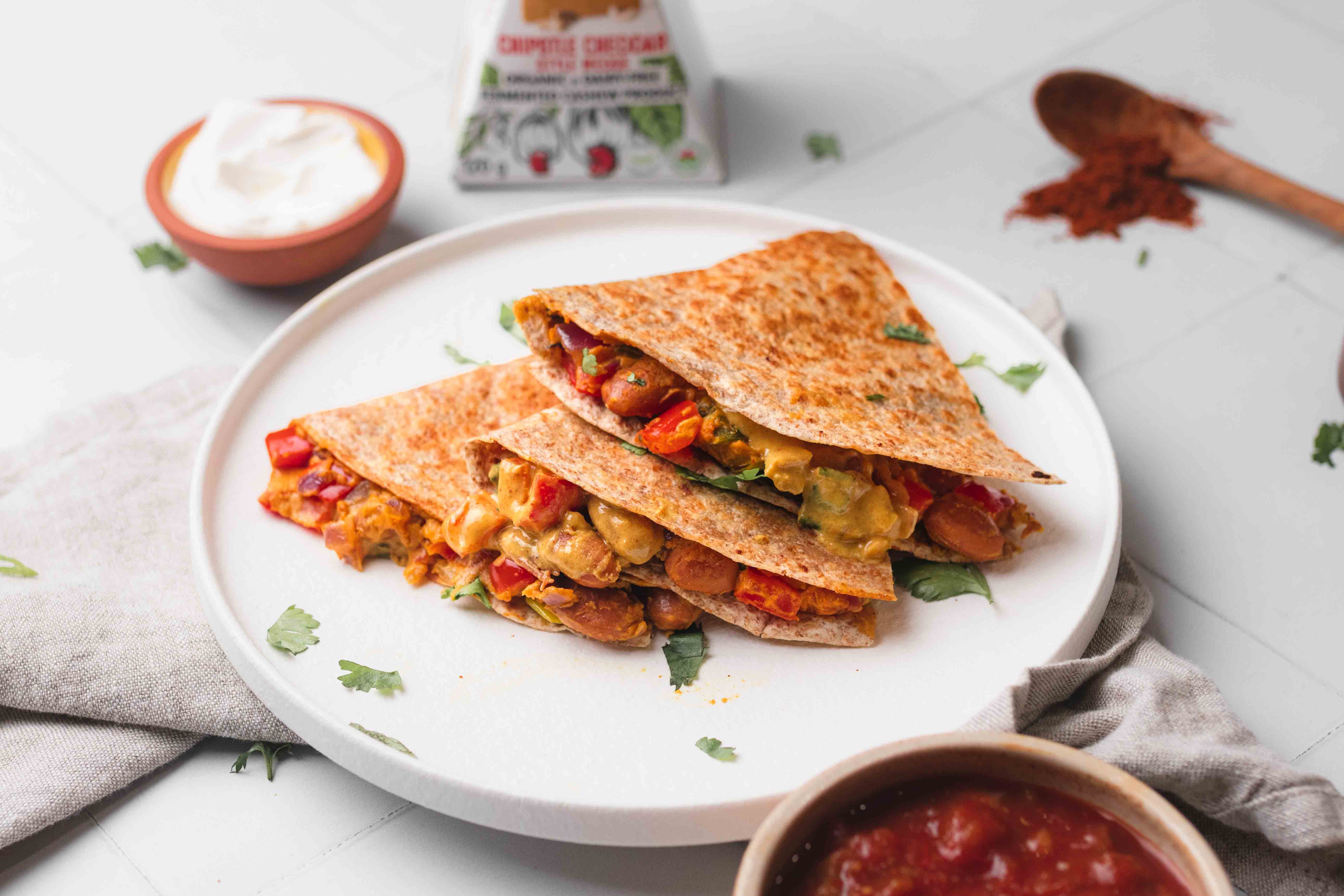 Préparation d'une quesadilla végétalienne aux haricots avec du fromage sans lait chipotle cheddar, accompagnée de salsa et de crème aigre sans lait.