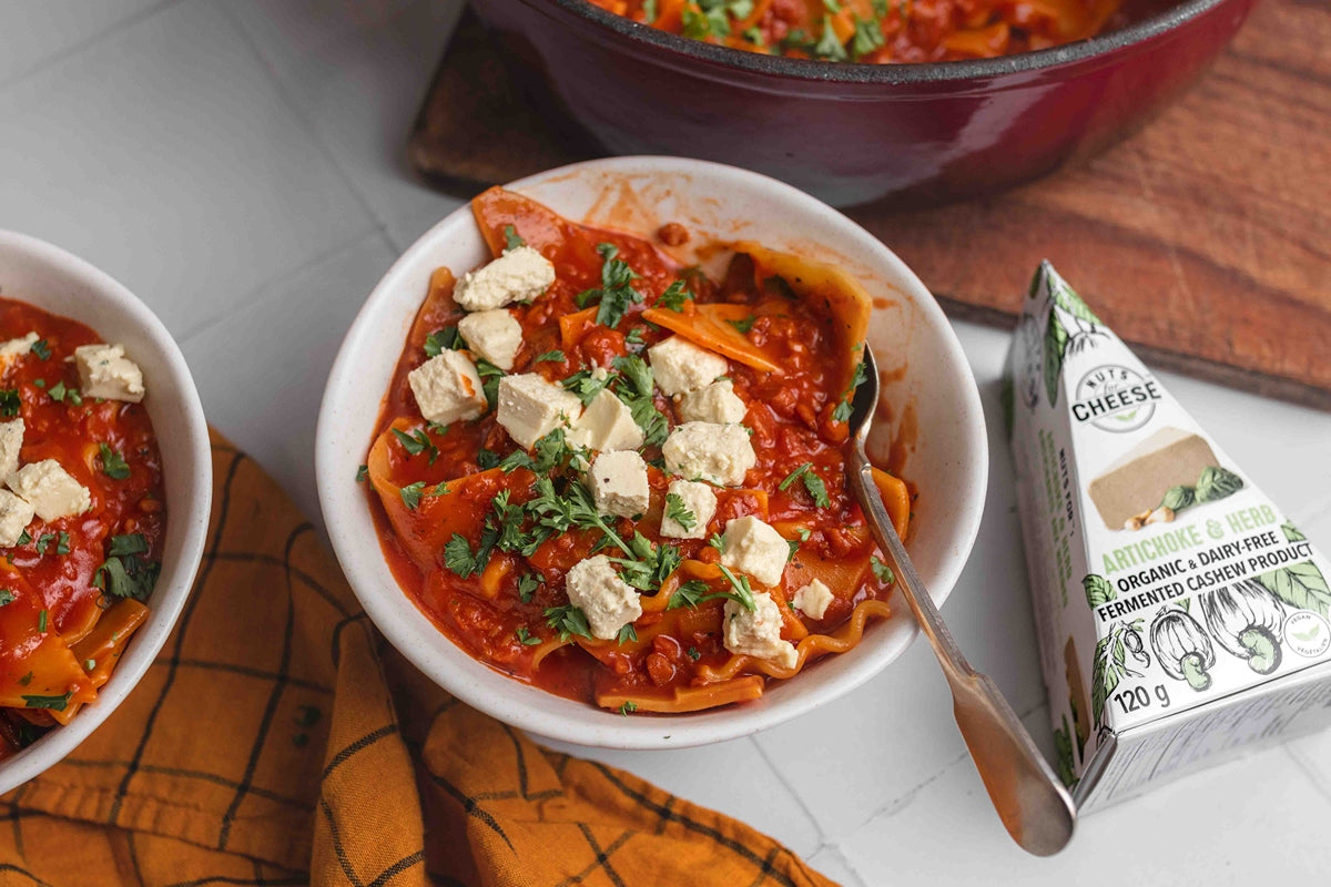 Un bol de soupe de lasagnes végétaliennes garni de morceaux d'artichauts sans produits laitiers et de fromage aux herbes.