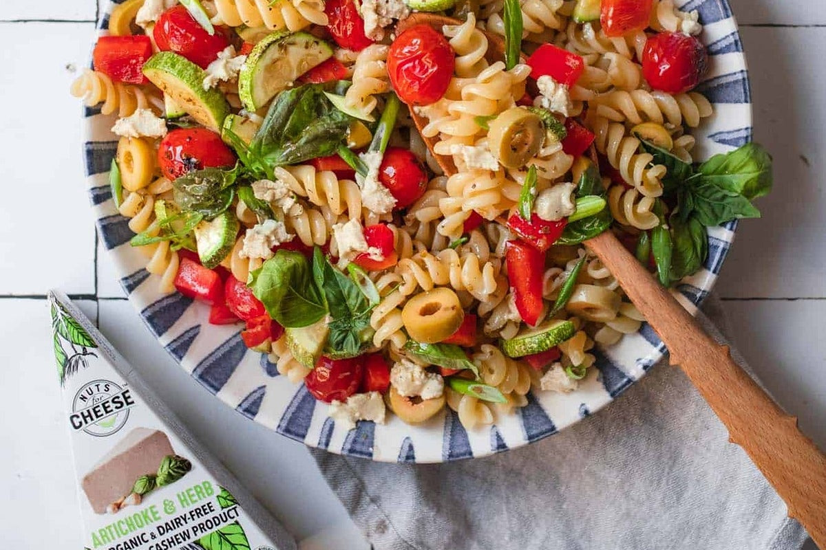 Grand bol de salade de pâtes végétalienne avec des légumes grillés et des morceaux d'artichauts et de fromage aux herbes sans produits laitiers.