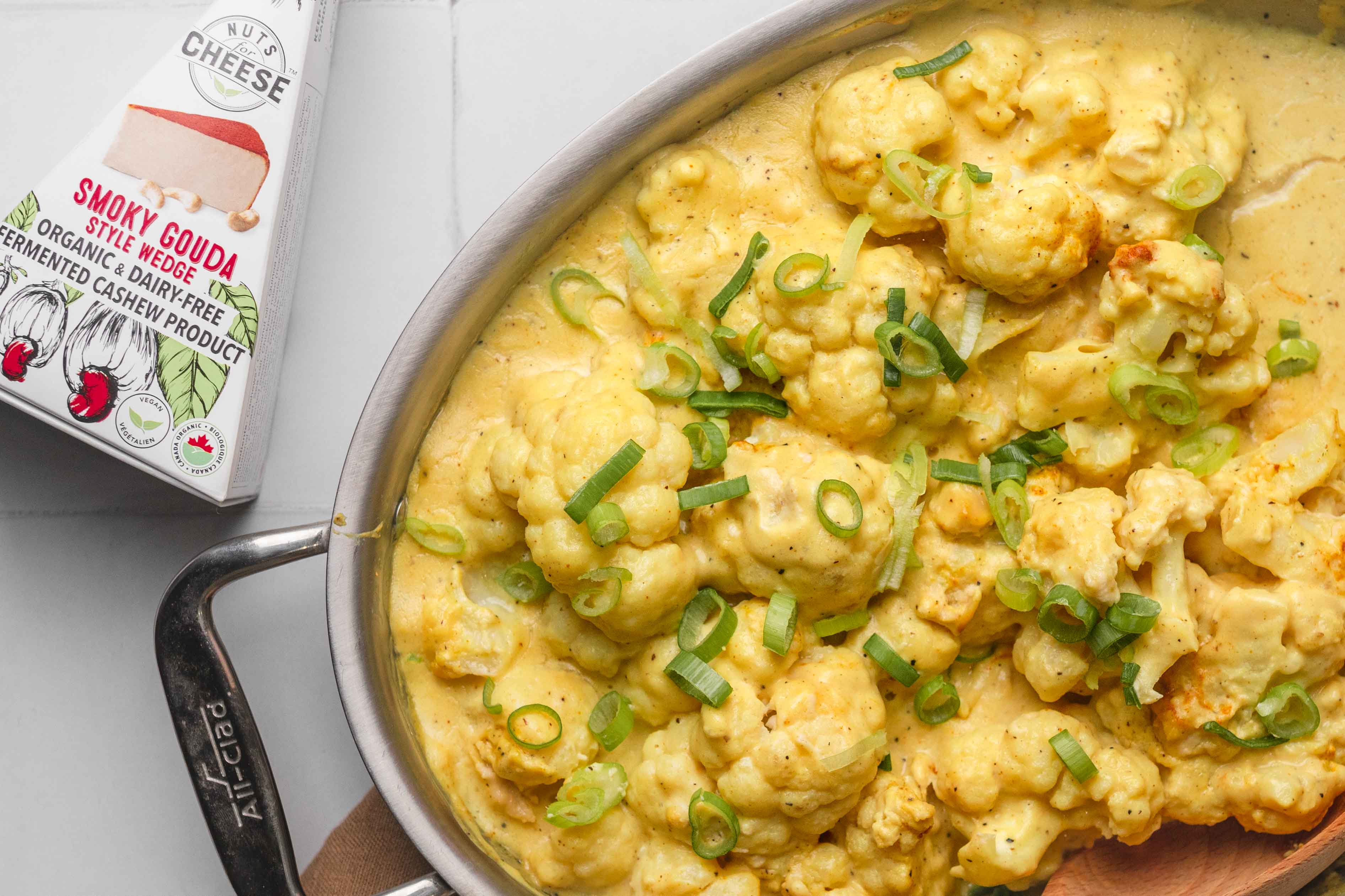 Poêle remplie de chou-fleur cuit au four dans une sauce au fromage sans produits laitiers. Posez à côté d'une boîte de gouda sans produits laitiers.