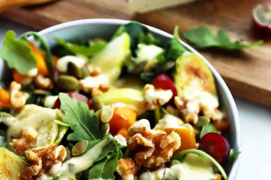 Bol de salade Waldorf comprenant des légumes frais, des choux de Bruxelles rôtis, des noix, des raisins et du fromage bleu sans produits laitiers.