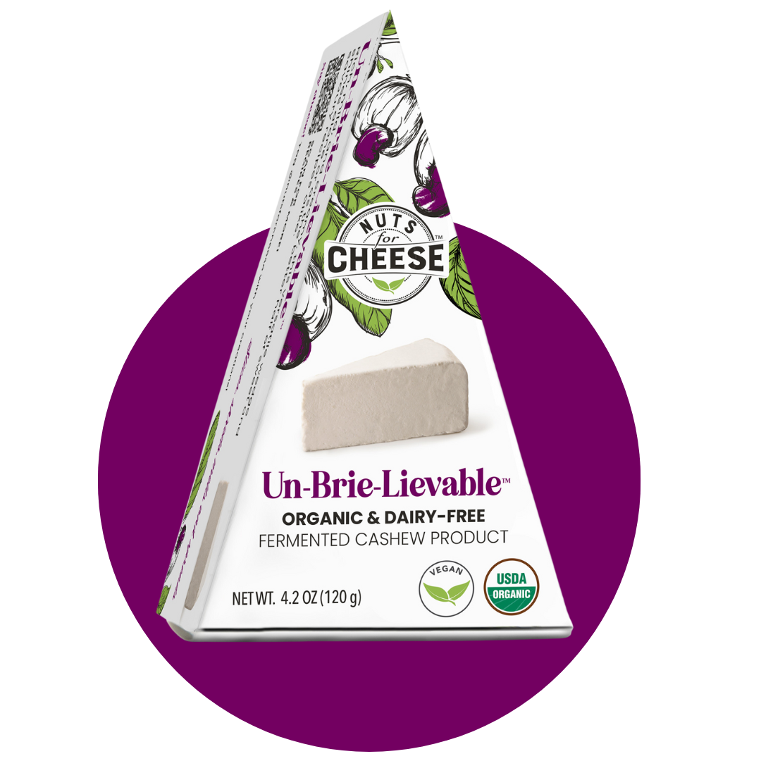 Nuts For Cheese™ Emballage de coins de fromage Brie Un-Brie-Lievable™ fermenté biologique et sans produits laitiers sur un fond de cercle violet.