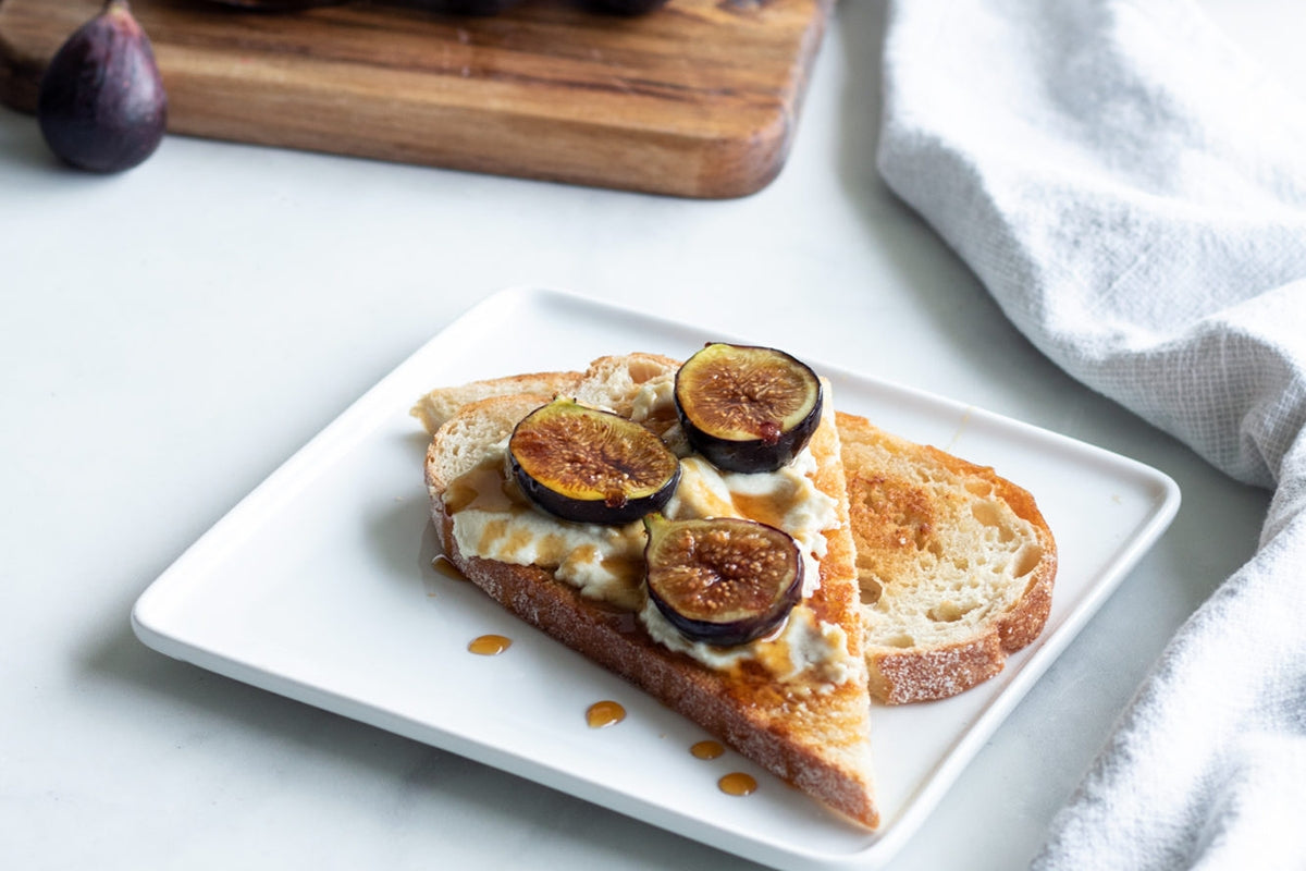 Toast au levain sur une assiette, garni de fromage brie végétalien et de tranches de figues fraîches.
