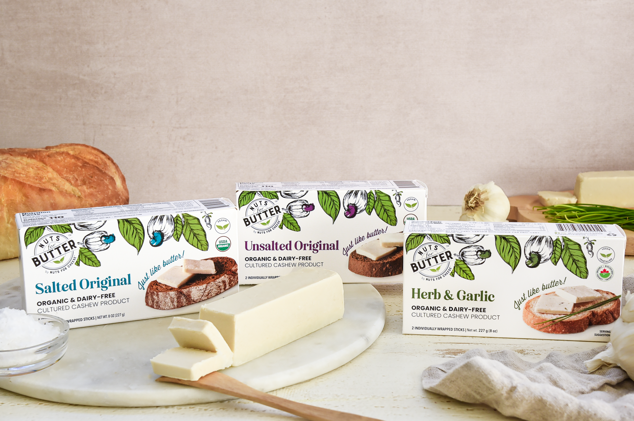 Les emballages de beurre sans produits laitiers de Nuts For Butter se trouvent à côté d'une barre de beurre végétal tranchée sur une planche de marbre.