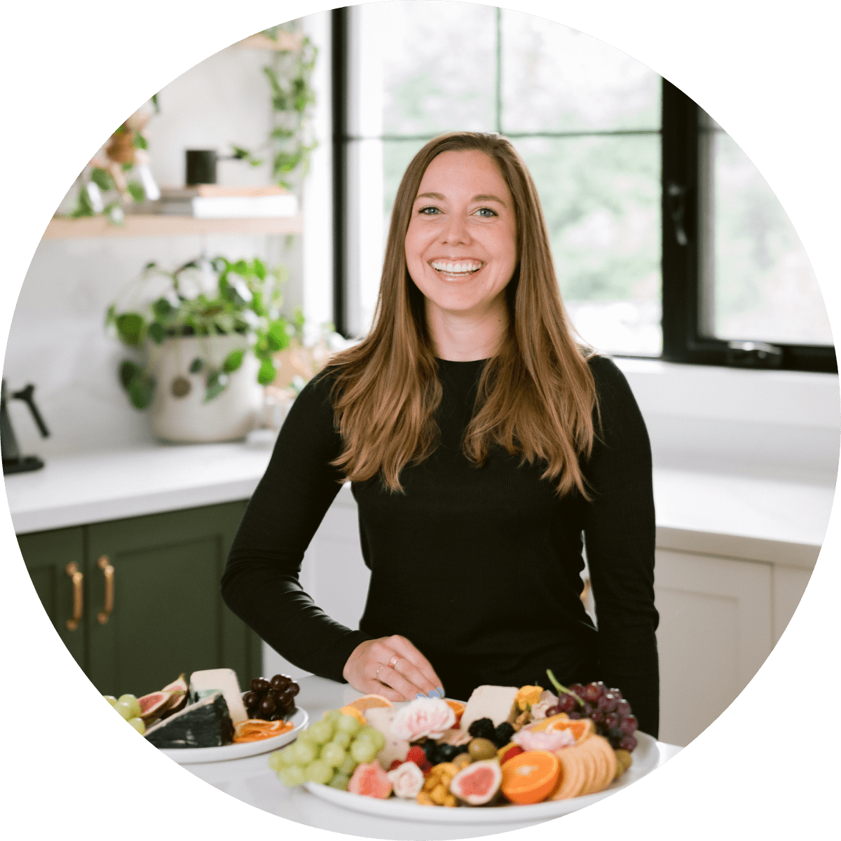 La fondatrice de Nuts For Cheese, Margaret Coons, souriant dans une cuisine derrière une assiette de fromage végétalien et de fruits frais.